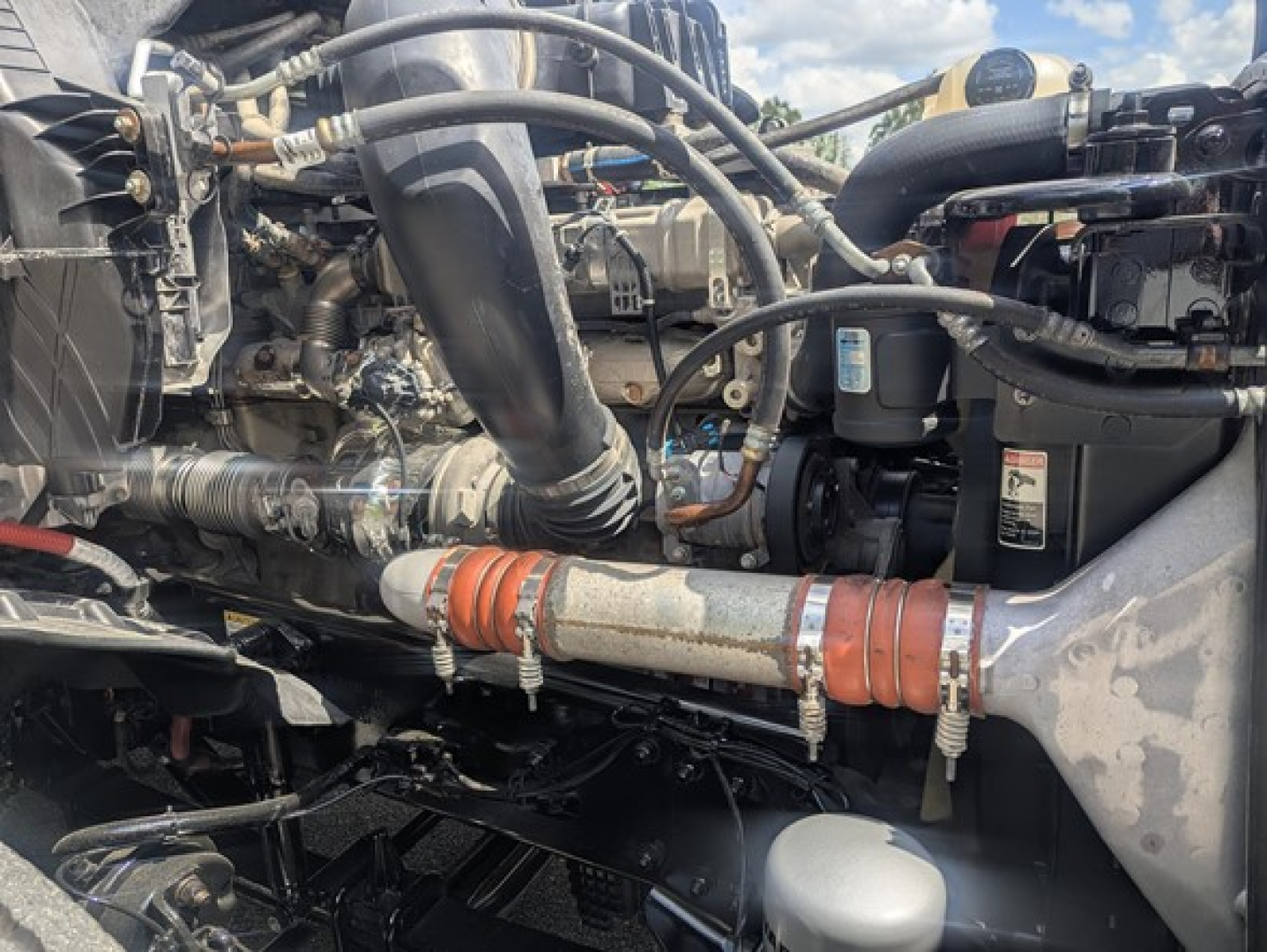 Freightliner Cascadia engine bay showing hoses, turbo, and coolant lines with orange ribbed hoses and clamps.