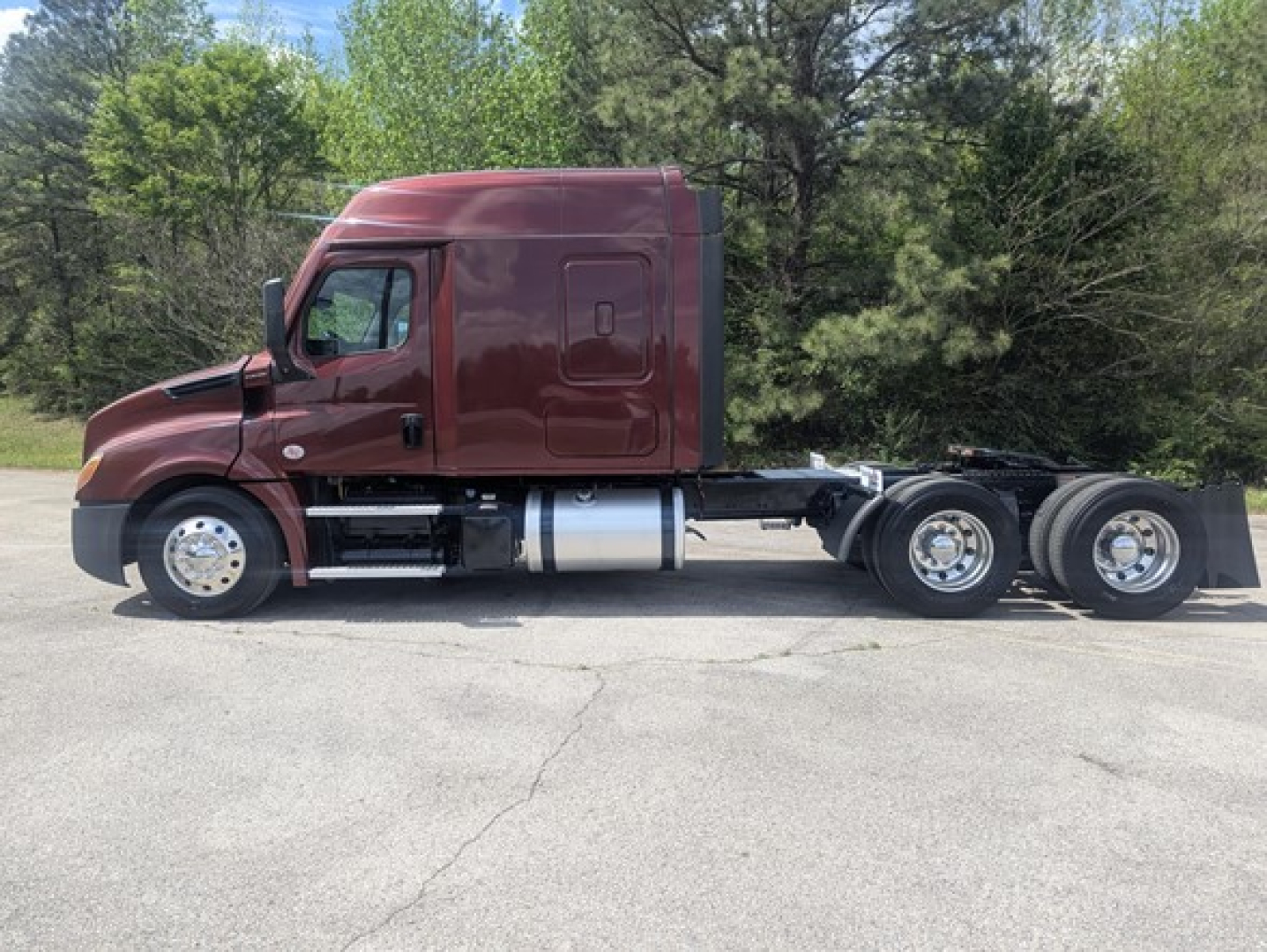 Truck side view showing a maroon 2022 Freightliner Cascadia 126 conventional sleeper with twin rear axles and fuel tanks.