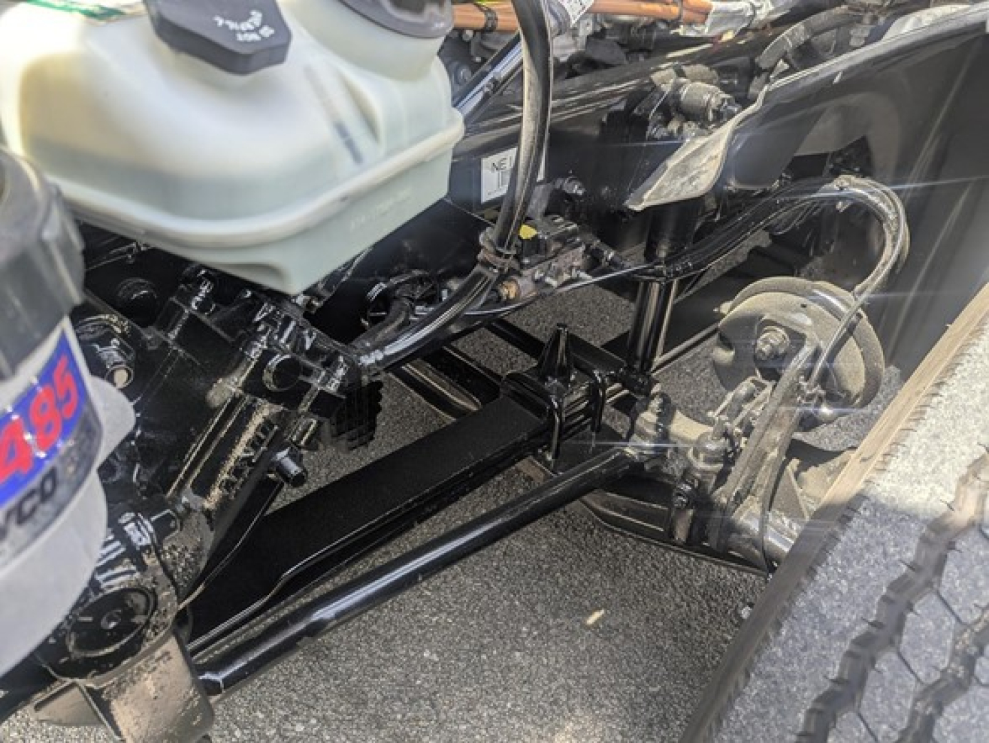 Freightliner Cascadia 126 frame and suspension components visible under front of truck. Hydraulic lines, steering linkage, and coolant reservoir visible.