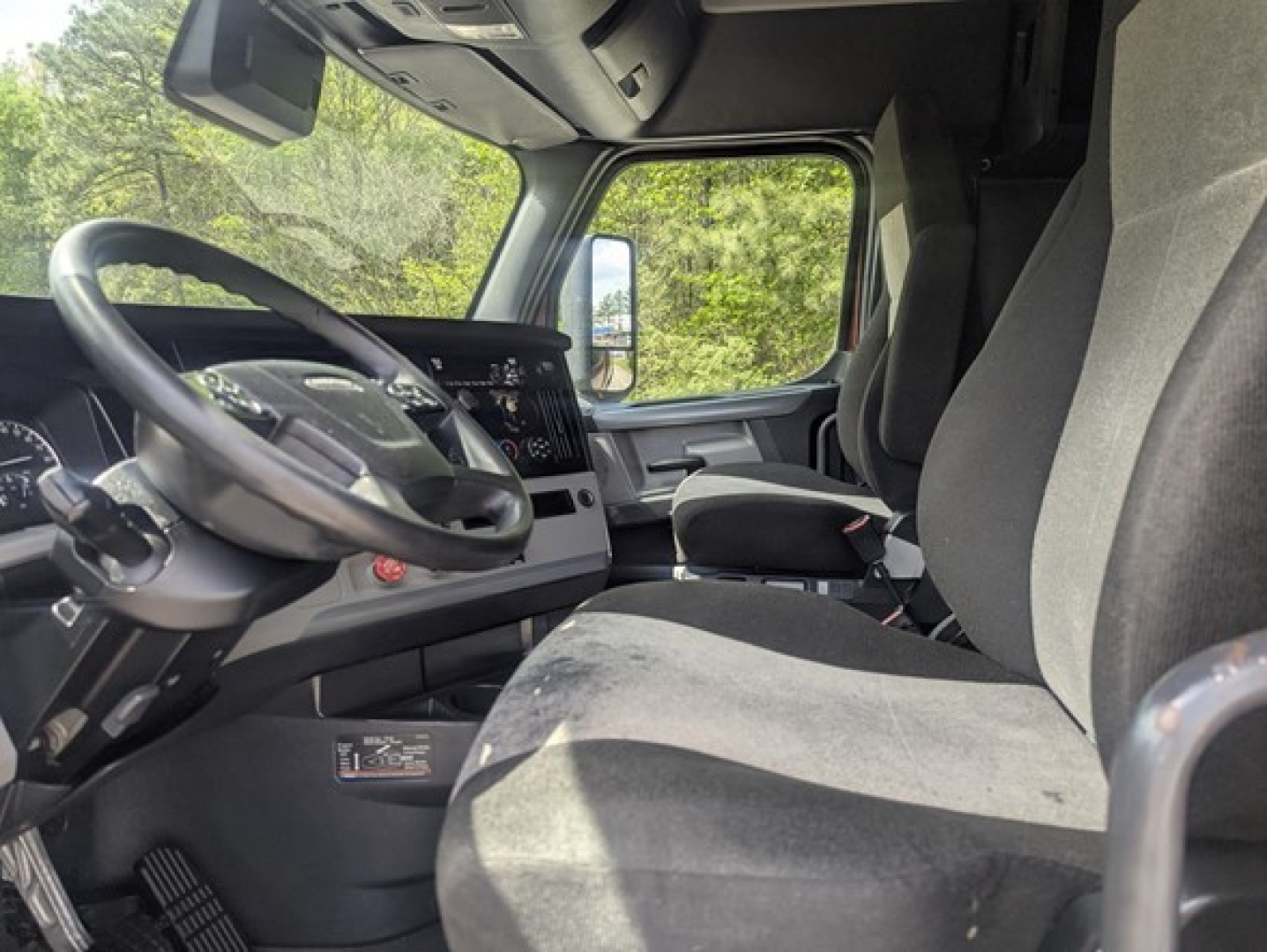 Truck cab interior showing steering wheel and dashboard of a Freightliner Cascadia with grey seats and modern instrument cluster.