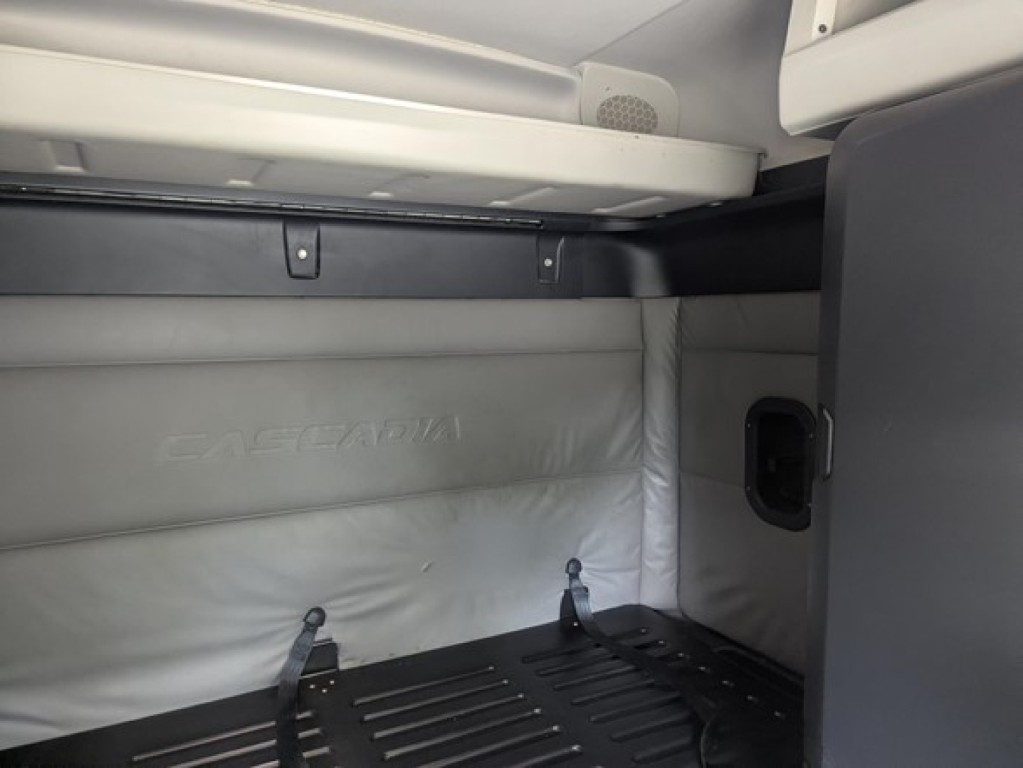Freightliner Cascadia cab interior showing sleeper area with white padded wall and cargo area.