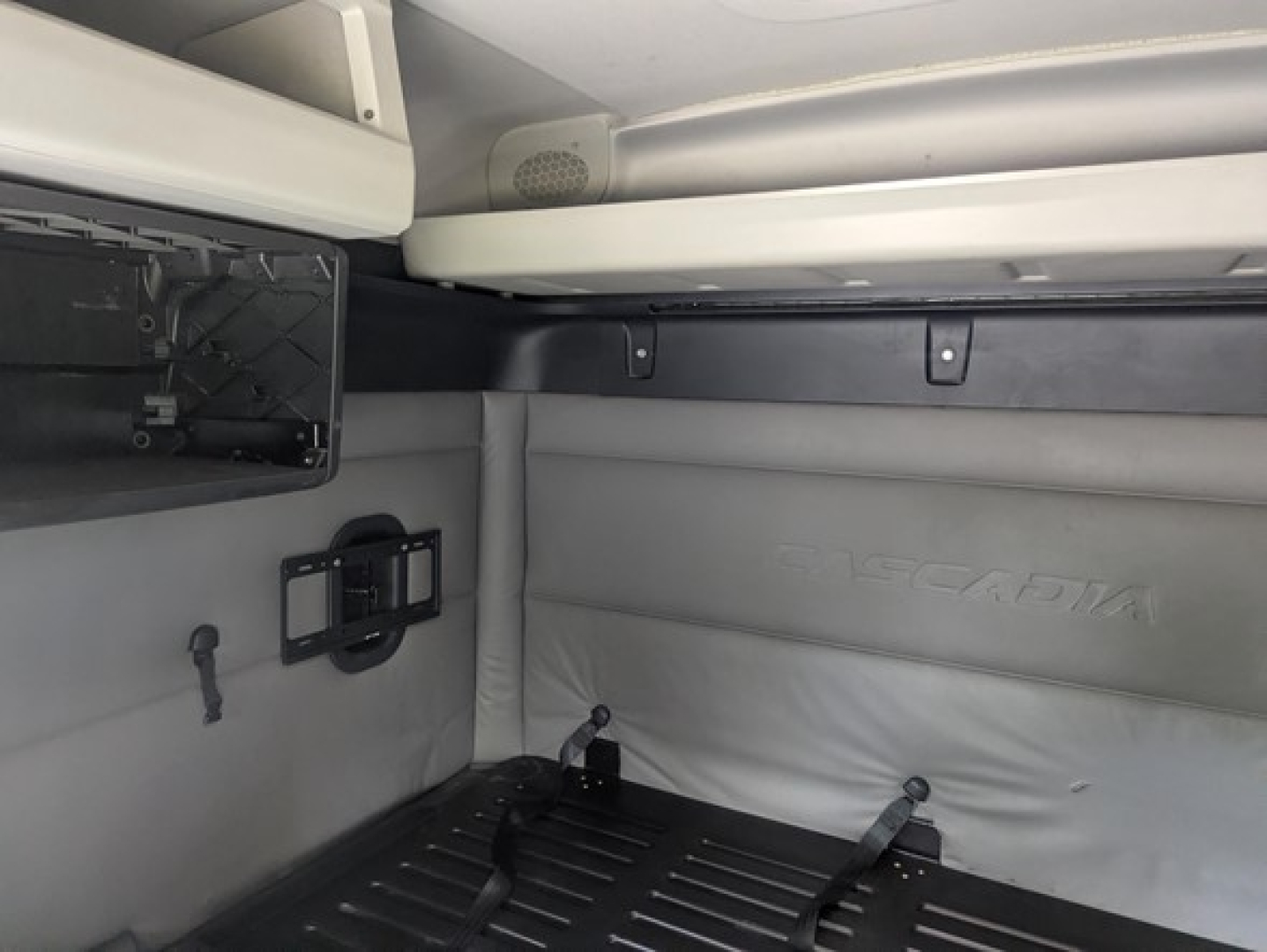 Freightliner Cascadia sleeper cab interior showing wall panel with embossed 'CASCADIA' and vehicle accessories; part of overhead storage and wall hooks visible.
