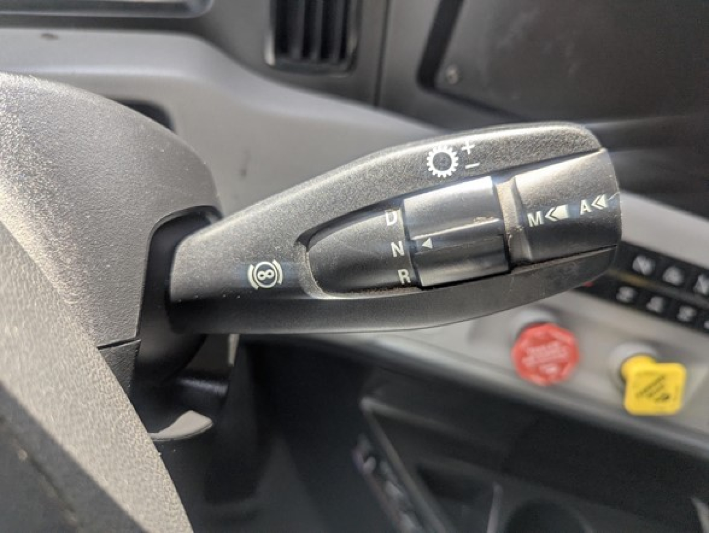 Truck steering column stalks with buttons and rotary dial visible in cab. Includes symbols for turn signals, cruise control, and lights.