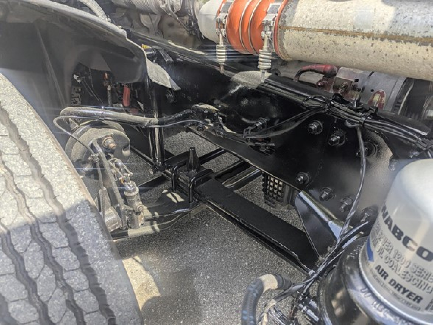 Freightliner Cascadia undercarriage showing suspension beams and hydraulic lines with engine bay components visible.