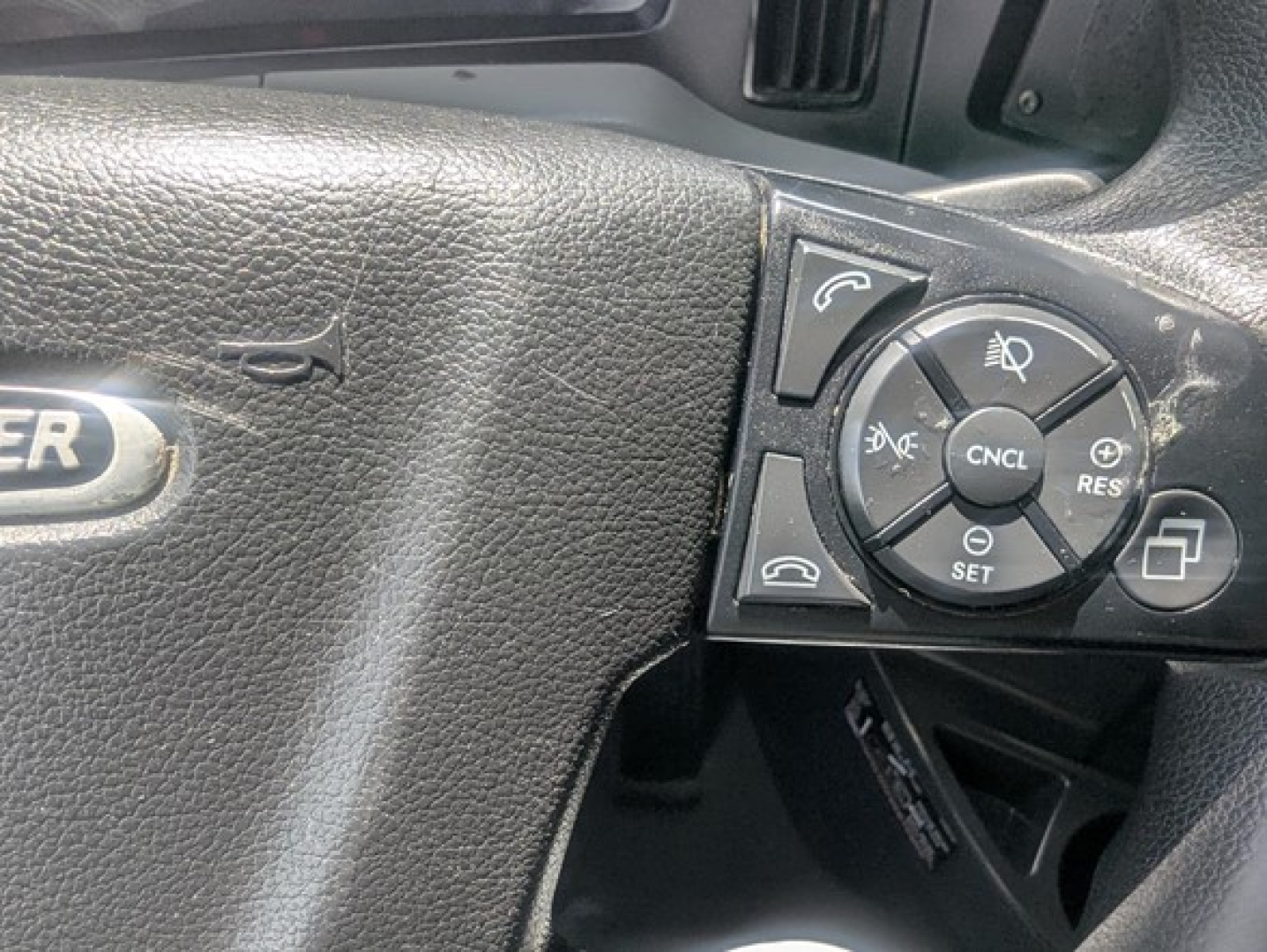 Freightliner steering wheel controls close-up showing cruise control buttons and CNCL/RES/SET along with stalks.