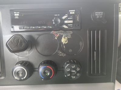Dashboard panel of a Freightliner Cascadia 126 truck showing climate controls, cigarette lighter, and media head unit with a damaged circular component area.