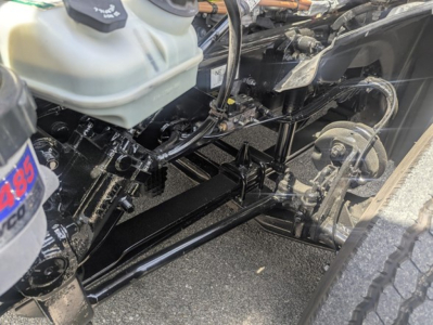 Freightliner Cascadia 126 frame and suspension components visible under front of truck. Hydraulic lines, steering linkage, and coolant reservoir visible.