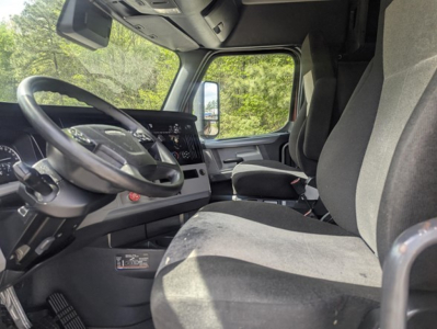 Truck cab interior showing steering wheel and dashboard of a Freightliner Cascadia with grey seats and modern instrument cluster.