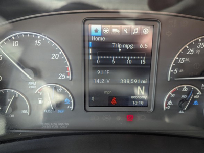Dashboard display of a 2022 Freightliner Cascadia showing trip mpg, engine metrics, and mileage in 388,591 mi; center touchscreen with Home and icons; left tachometer and right speedometer.
