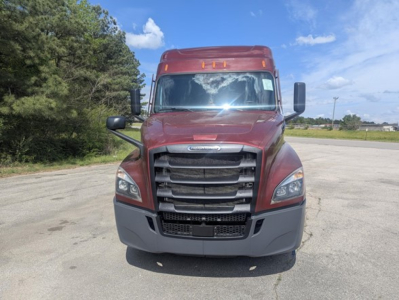 Freightliner Cascadia front view showing bold black grille, maroon cab, large side mirrors, and bumper; daytime clear sky and open lot background.
