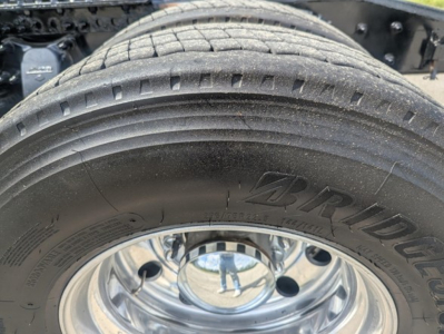 Tire and wheel of a Freightliner Cascadia truck showing BRIDGESTONE tire tread and chrome rim; part of the rear axle area visible.