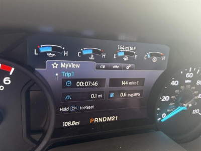 Truck instrument cluster display showing trip details: 00:07:46 duration, 0.1 mi, 0.6 avg MPG, 144 mi to E, PRNDM21 gear indicator, and MyView Trip1 on screen.