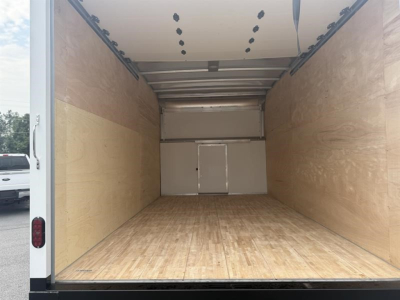 Open cargo area of a new 2027 Ford E450 with empty wooden floor and tall ceiling, rear doors closed, interior walls in light plywood.