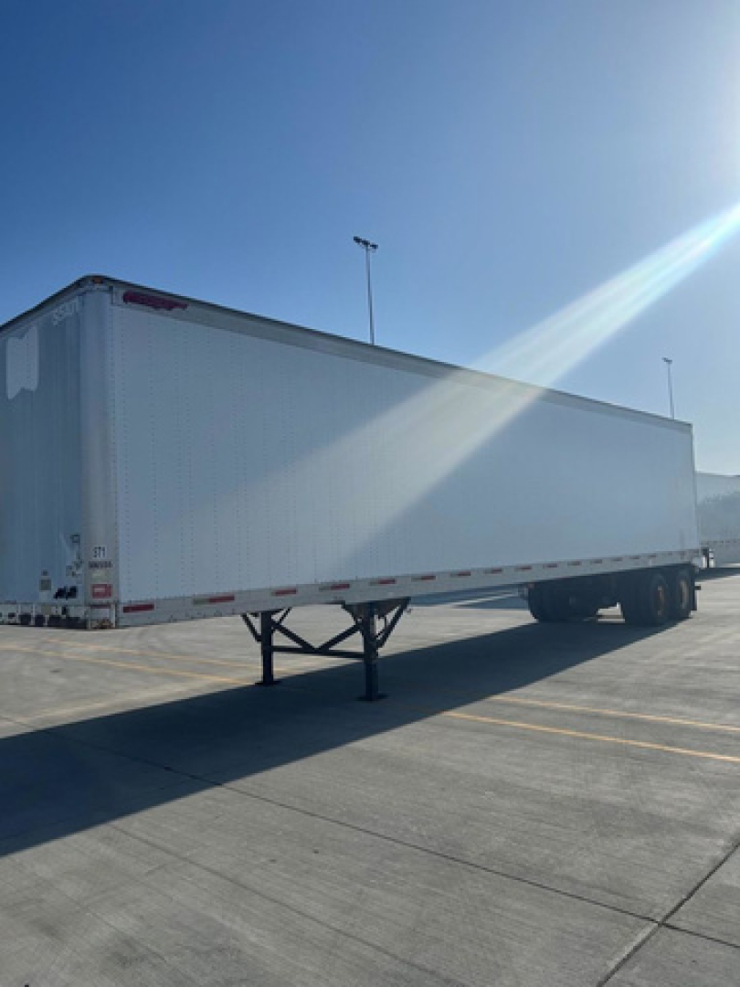 Trailer van side view showing a white Great Dane trailer with landing gear and front hitch, under clear sky.
