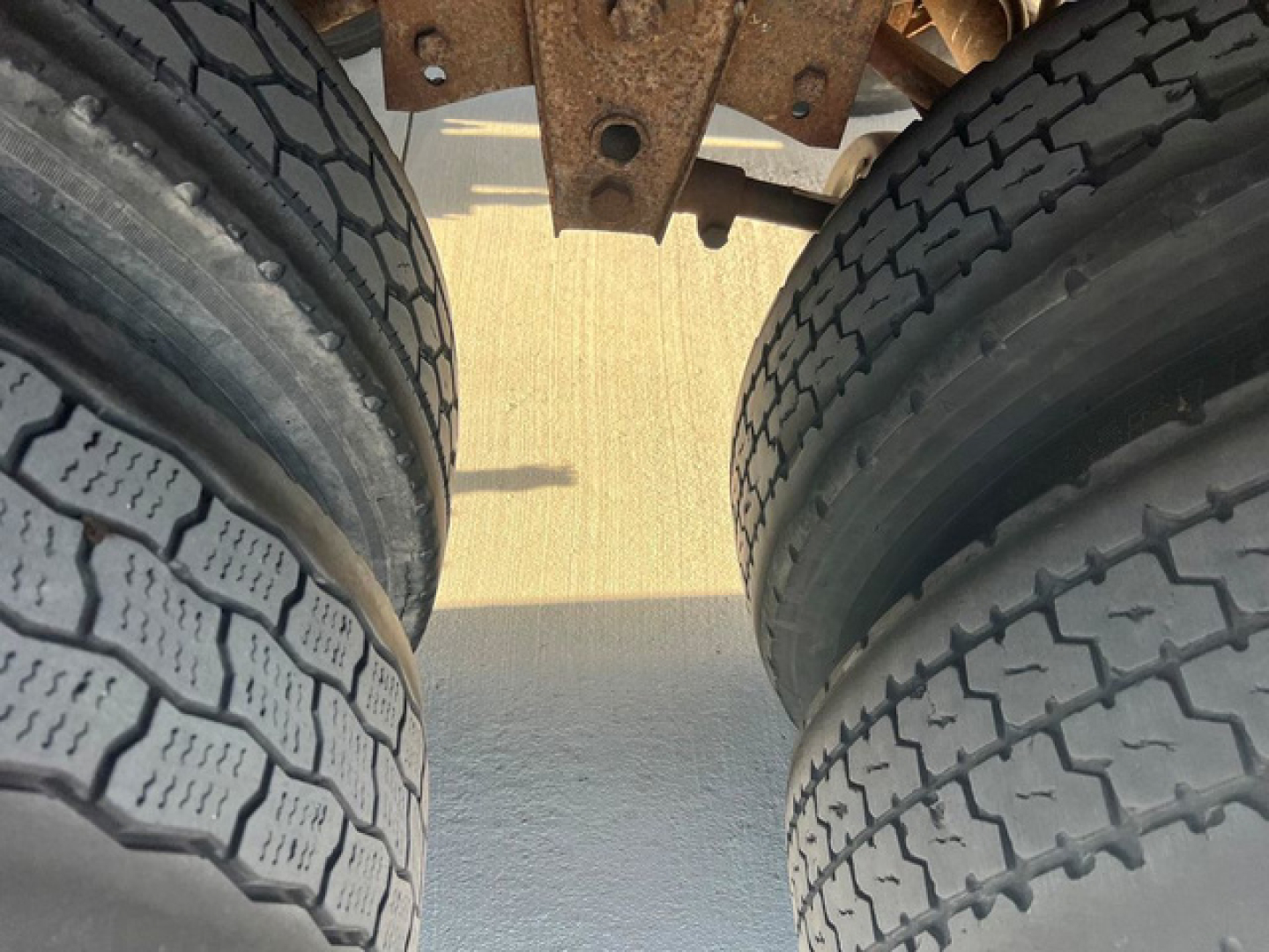 Dual rear tires of a trailer chassis, with metal frame above and shadows on ground.