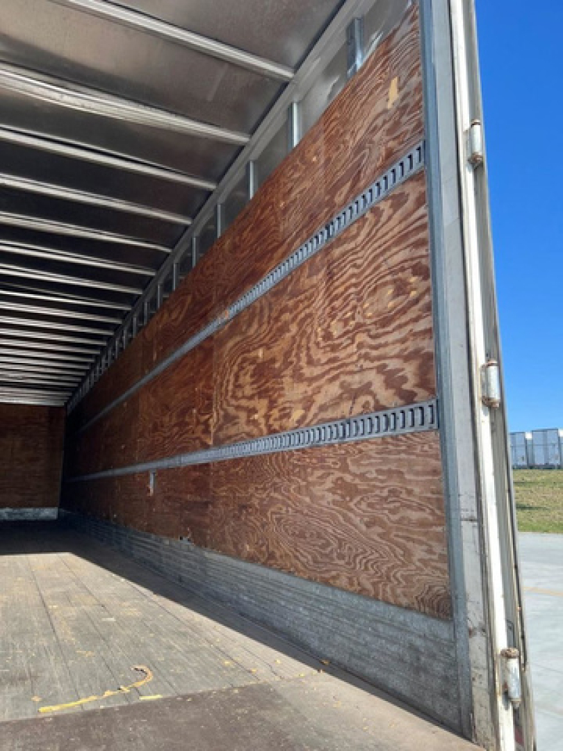 Trailer interior showing wooden side panels and metal rails with sunlight from open end.