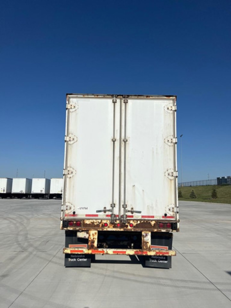 Rear view of a white Great Dane trailer with tall doors, rust spots on the lower rear frame, and a dark bumper section.