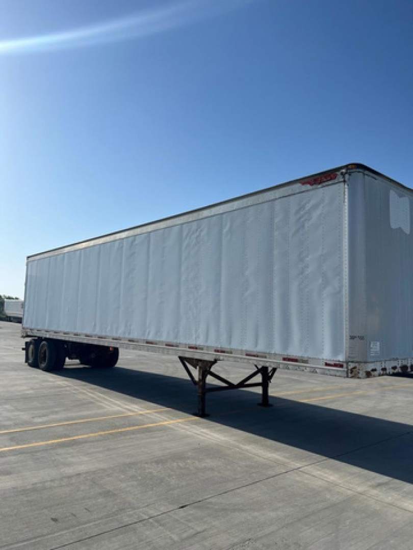 Trailer semitrailer docked showing long rectangular gray curtain side and landing gear.