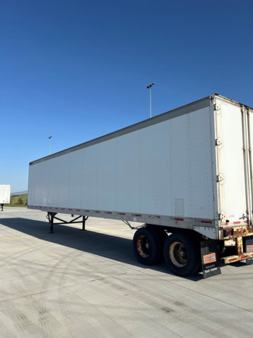 Trailer side view showing a white Great Dane van trailer with dual rear wheels and flatbed undercarriage.