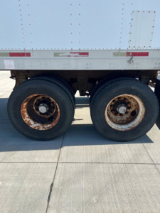 Dual rear trailer wheels with rusted rims under a Great Dane trailer side. Visible are no legible labels or numbers, just the wheel assembly and lower side of the trailer.
