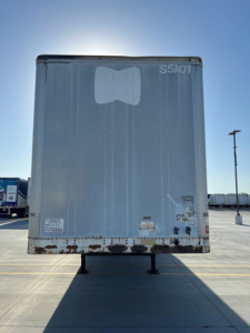 Rear view of a Great Dane trailer on a parking lot with weathered lower edge and raised legs.