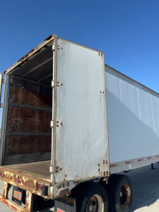 Trailer rear with open ramp showing cargo area and wooden interior, Great Dane van trailer in side view.