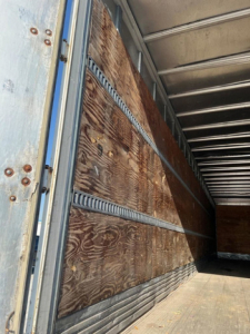 Van trailer interior showing wooden side walls and metal framing, viewed from doorway with plywood panels and cargo area.
