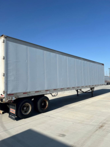 Trailer side view showing a long gray Great Dane van trailer with dual rear axles and black mud flaps.