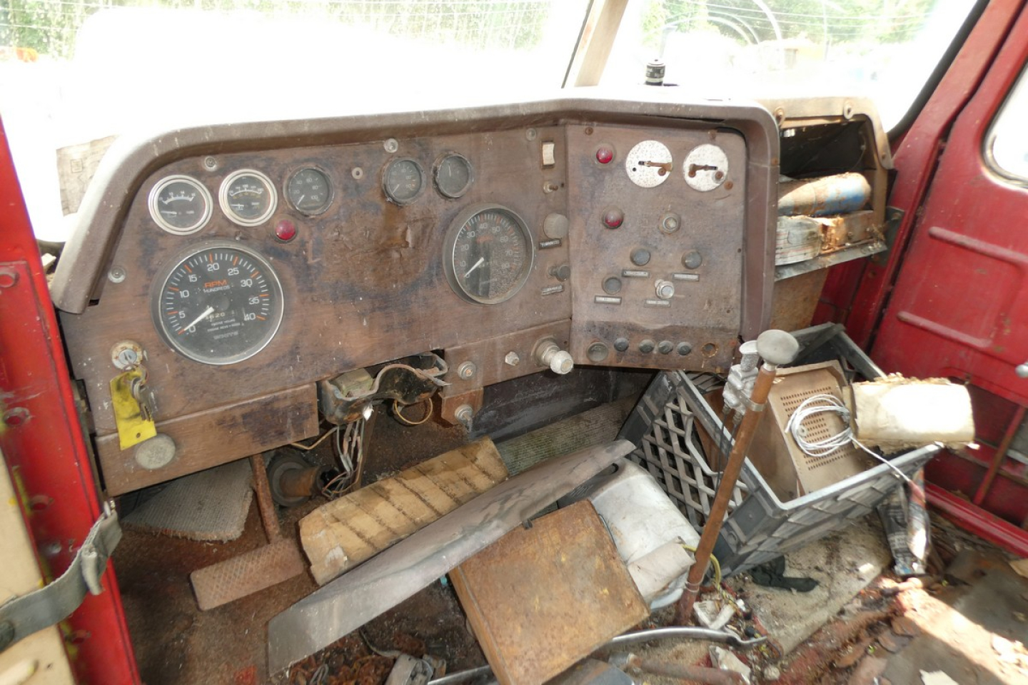 Dashboard of an older day cab truck with analog gauges, rusted panel, and exposed wiring; visible labels include gauges and switches but no clear legible text.