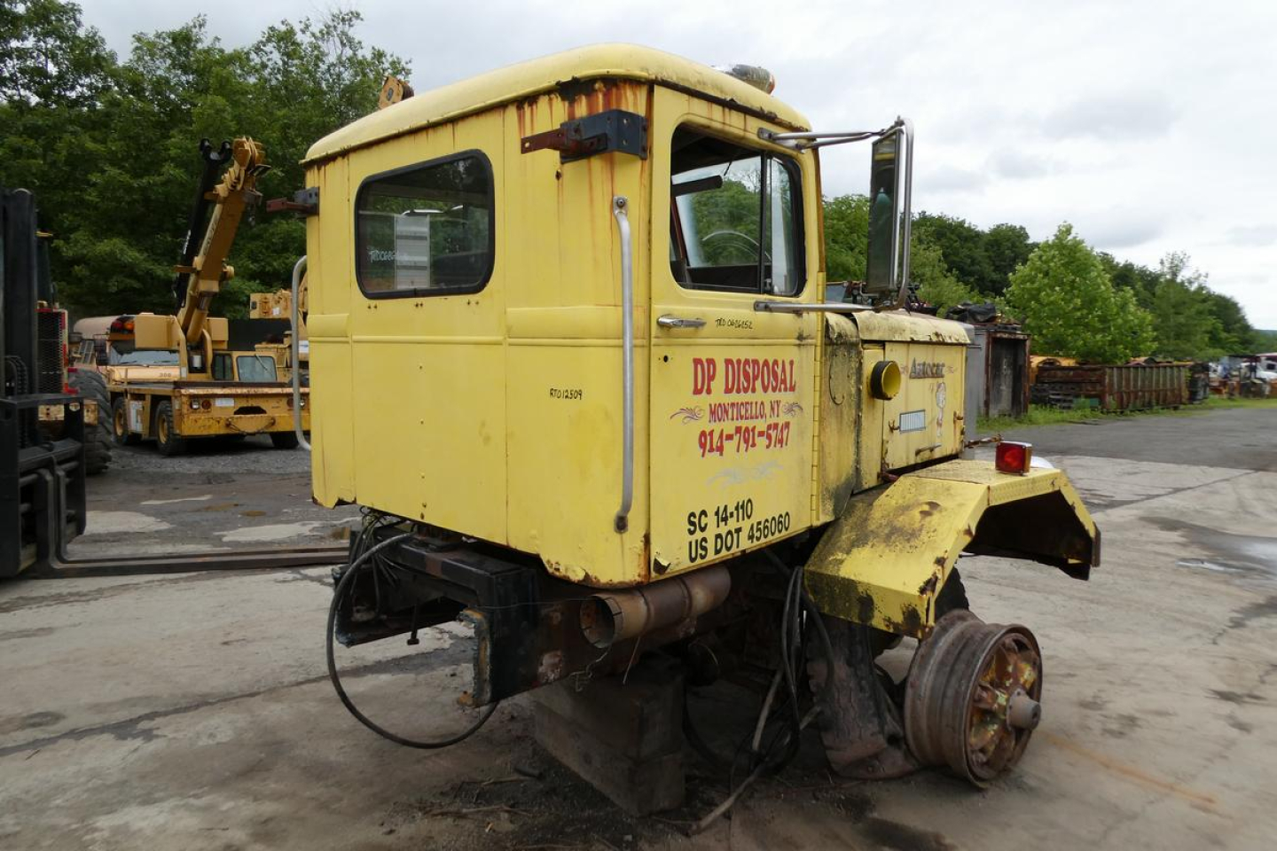 1973 Autocar cab cut truck cab with yellow paint, side text reading DP Disposal and contact numbers, rear wheel removed, in salvage yard