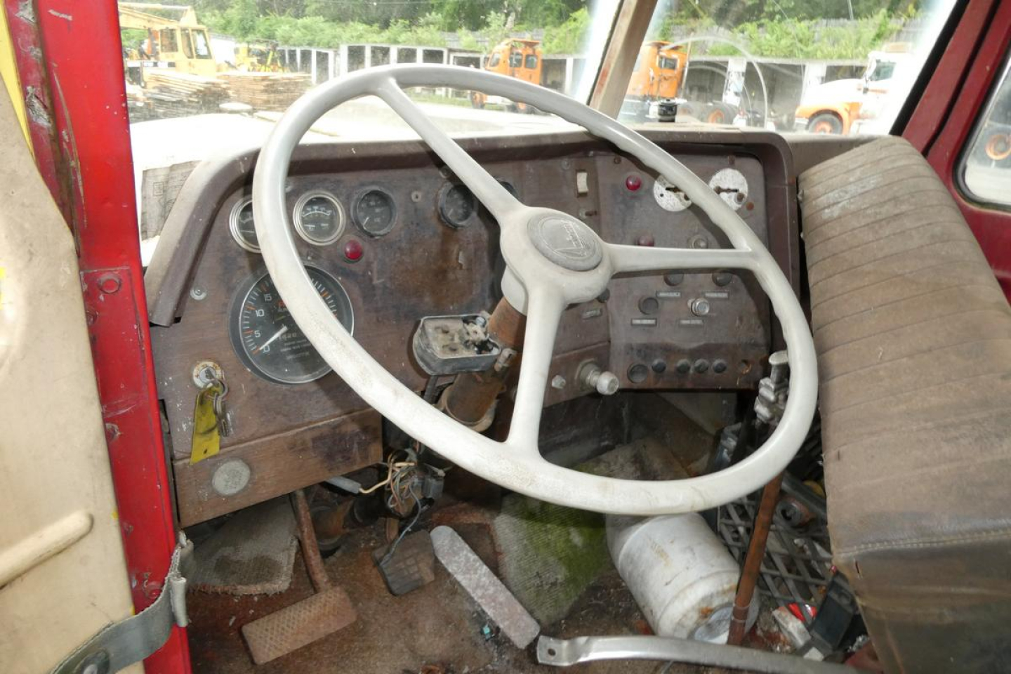 Cab interior of an old Autocar day cab showing steering wheel and rusted dashboard gauges.