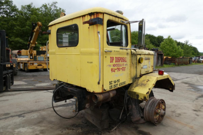 1973 Autocar cab cut truck cab with yellow paint, side text reading DP Disposal and contact numbers, rear wheel removed, in salvage yard
