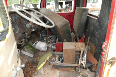 Interior of a 1973 Autocar cab cut showing steering wheel, dashboard, and cluttered floor with old equipment and wiring.