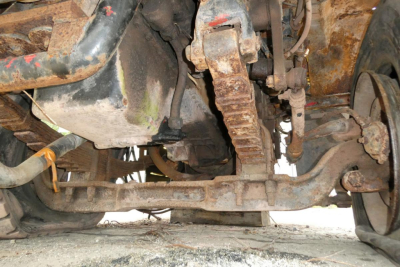Underbody of a 1973 Autocar cab showin suspension components, rusty frame, and drivetrain parts visible.