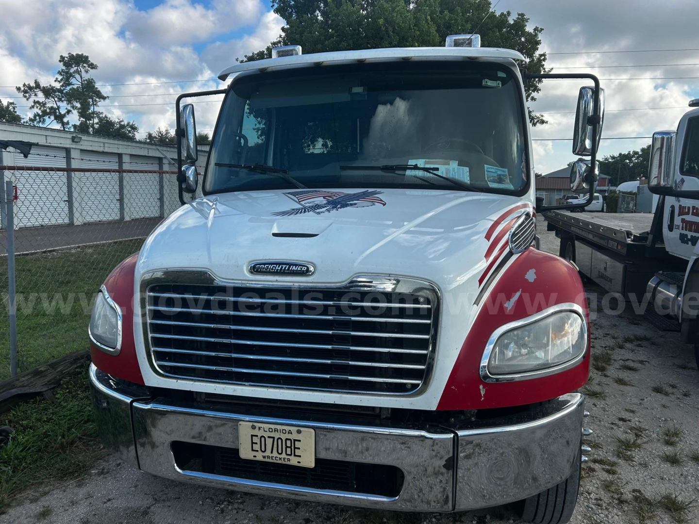 Front view of a 2018 Freightliner M2 tow truck showing chrome grille, headlights, and red fender accents; license plate E070BE on front bumper.