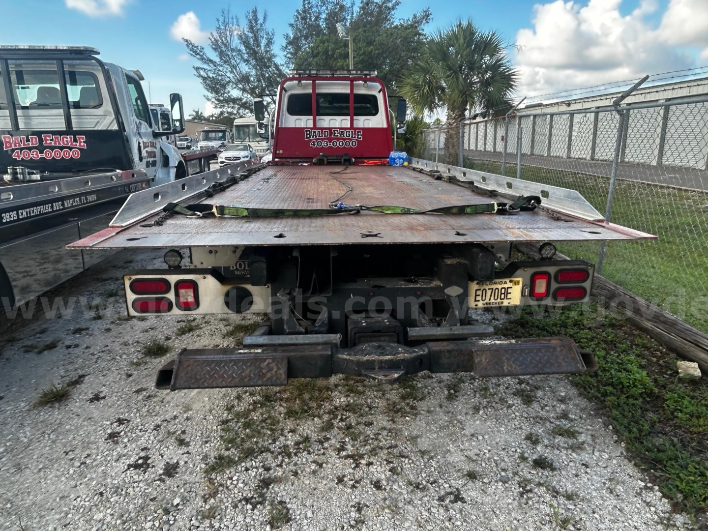 Flatbed tow truck bed rear view showing license plate E07BE on bumper and dual taillights.