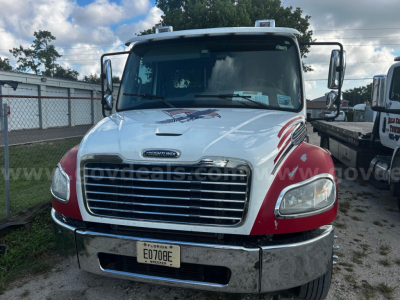 Front view of a 2018 Freightliner M2 tow truck showing chrome grille, headlights, and red fender accents; license plate E070BE on front bumper.