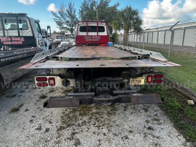 Flatbed tow truck bed rear view showing license plate E07BE on bumper and dual taillights.