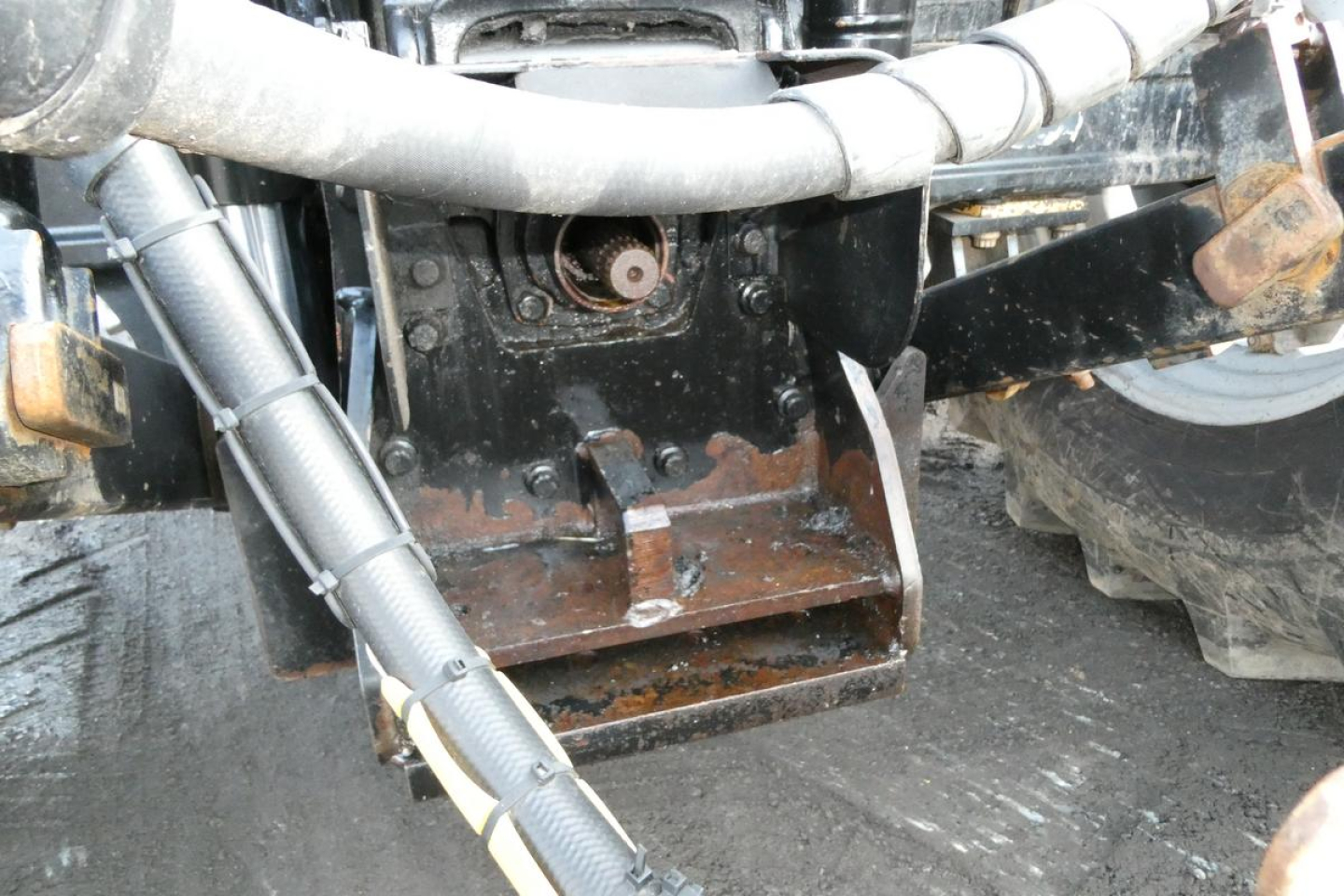 Tractor hitch and hydraulic components showing rusted steel bucket and hoses under a Challenger MT455B chassis.