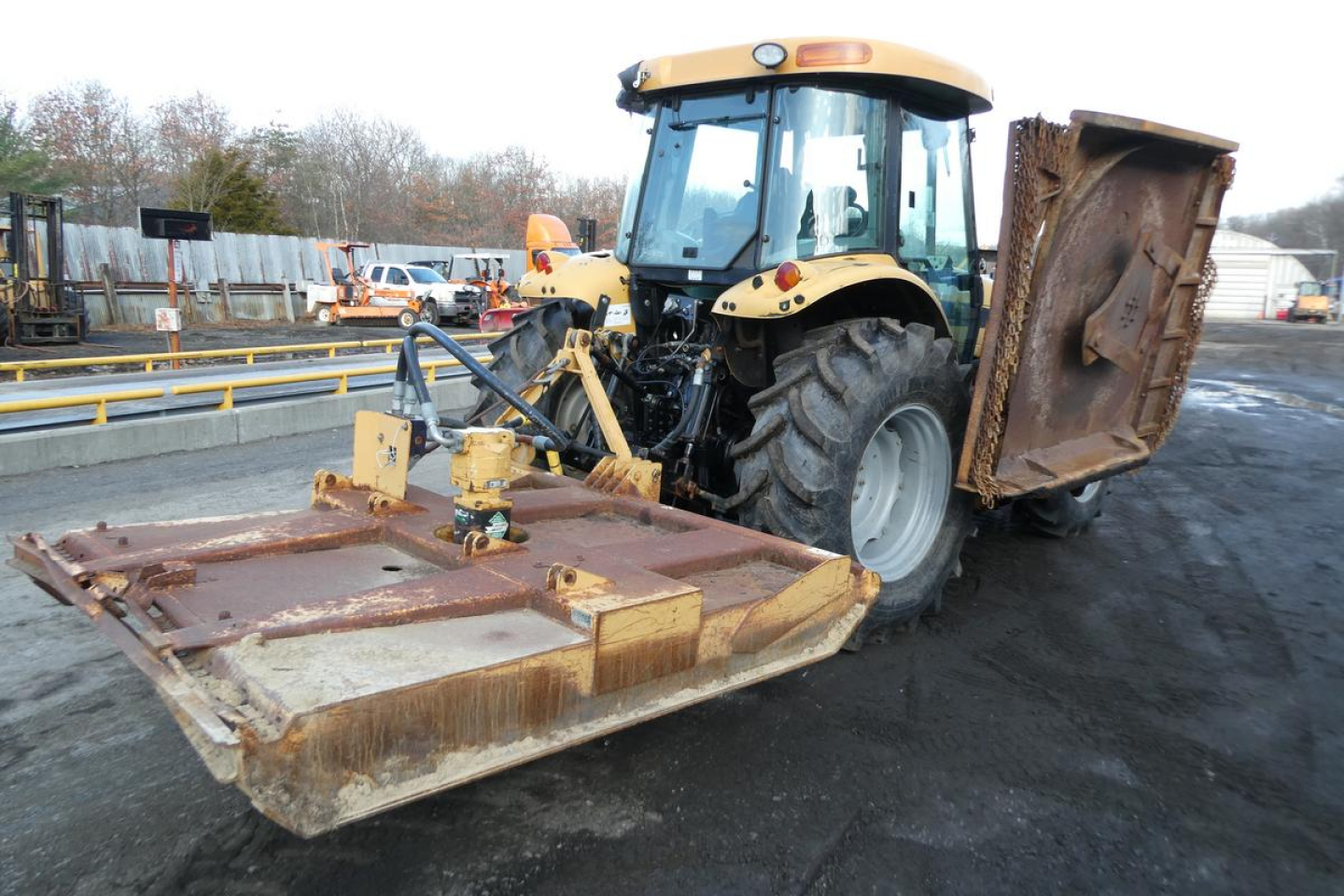 Tractor with front-mounted mower attachment in view showing yellow MT455B tractor and rusted cutting implement.