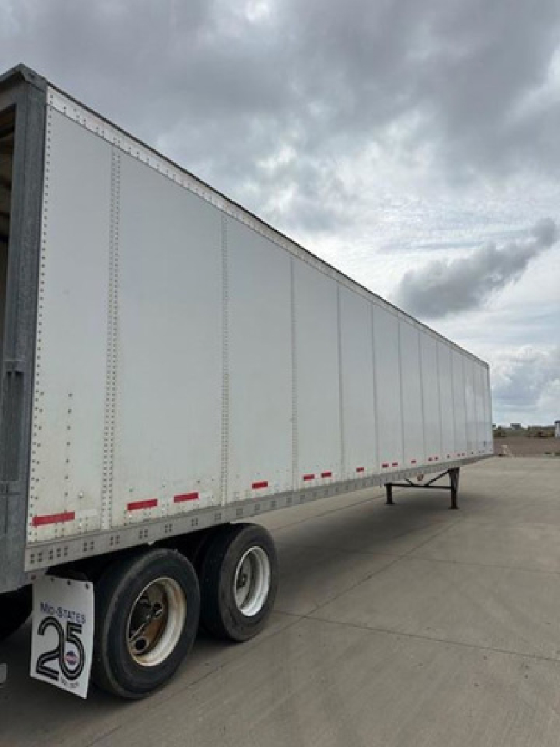 Trailer side view showing silver Wabash trailer with white reflective tape and dual rear wheels.