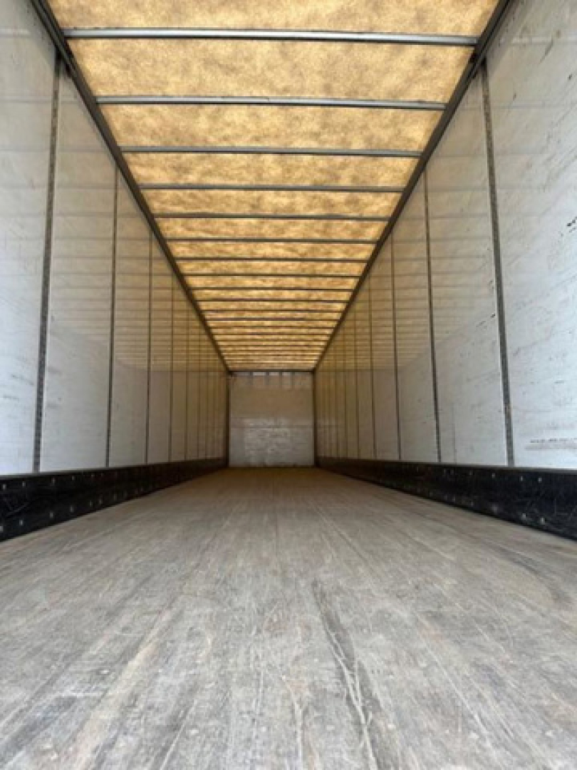 Trailer interior: empty Wabash van trailer cargo area with wooden roof paneling and side walls, long rectangular interior with metal beams and plywood ceiling.