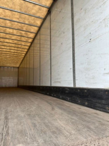 Trailer interior showing empty cargo space with wooden floor and side walls, long van trailer ceiling with ribbed framework.