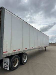 Trailer side view showing silver Wabash trailer with white reflective tape and dual rear wheels.