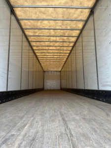 Trailer interior: empty Wabash van trailer cargo area with wooden roof paneling and side walls, long rectangular interior with metal beams and plywood ceiling.