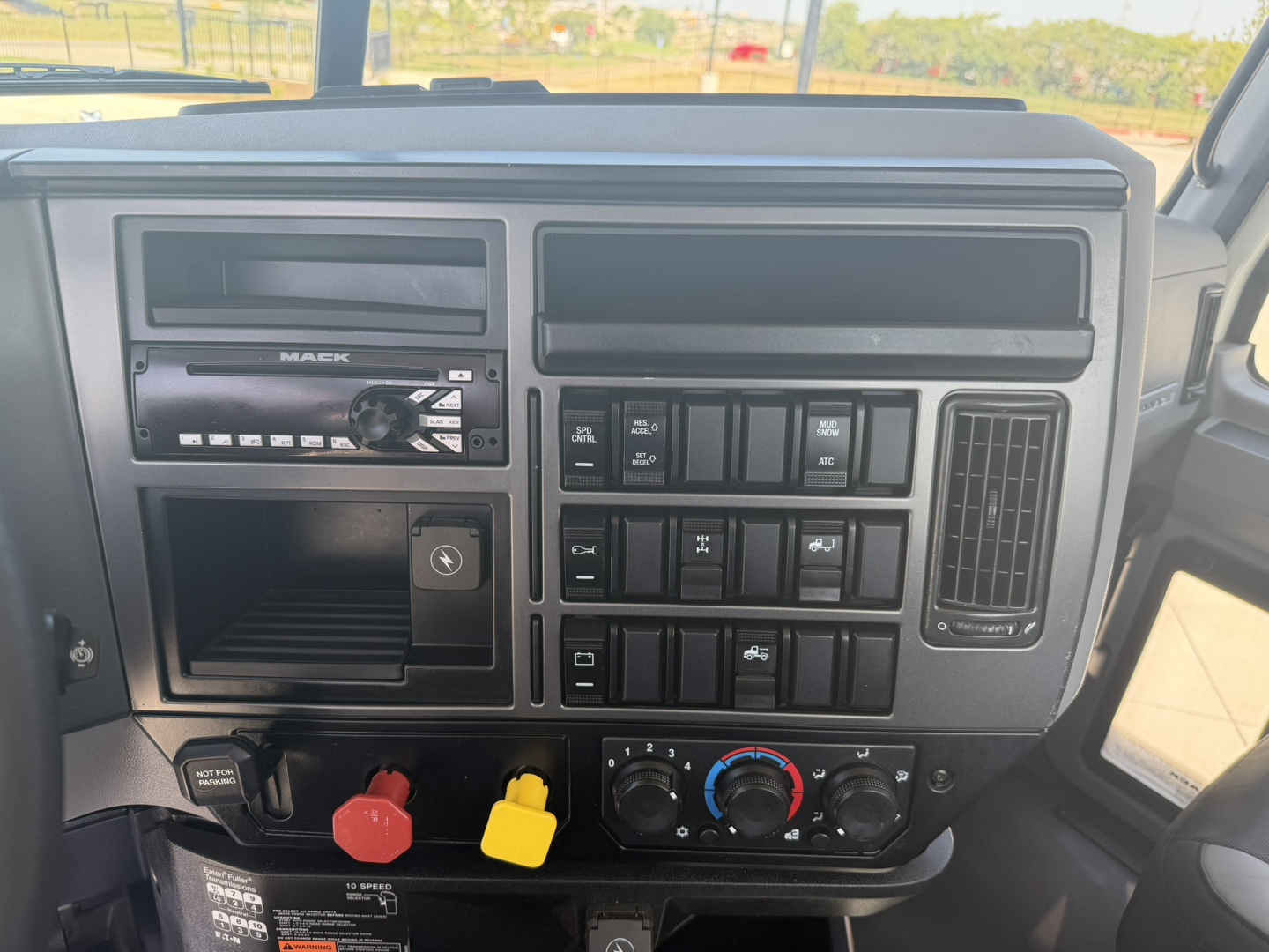 Mack PI64T truck cab dashboard showing steering column area with radio, control switches, and climate controls visible; red and yellow knobs; GFCI-style vents.