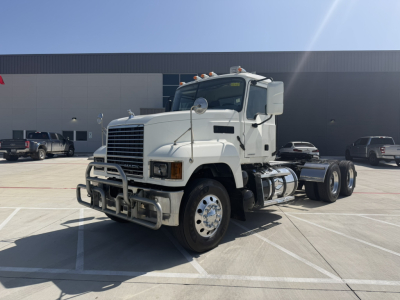 Truck cab exterior of a white 2020 Mack PI64T conventional daycab, front grille with bumper guard, dual rear axles, showing chrome wheels and fuel tanks.