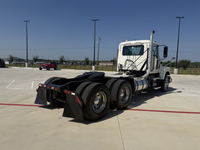 Truck tractor chassis with cab in front, back view showing fifth wheel and dual rear axles on a concrete lot; Mack PI64T branding not visible on side.