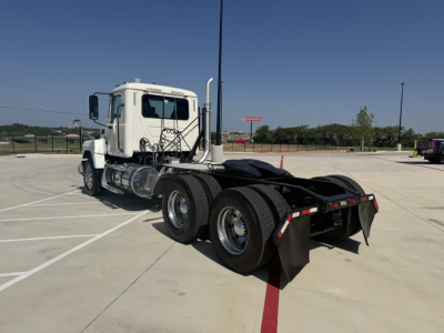 Truck cab and chassis of a 2020 Mack PI64T in a parking lot, side view showing rear dual-axle bogie and fifth-wheel attachment, with fuel tanks and exhaust stack visible.