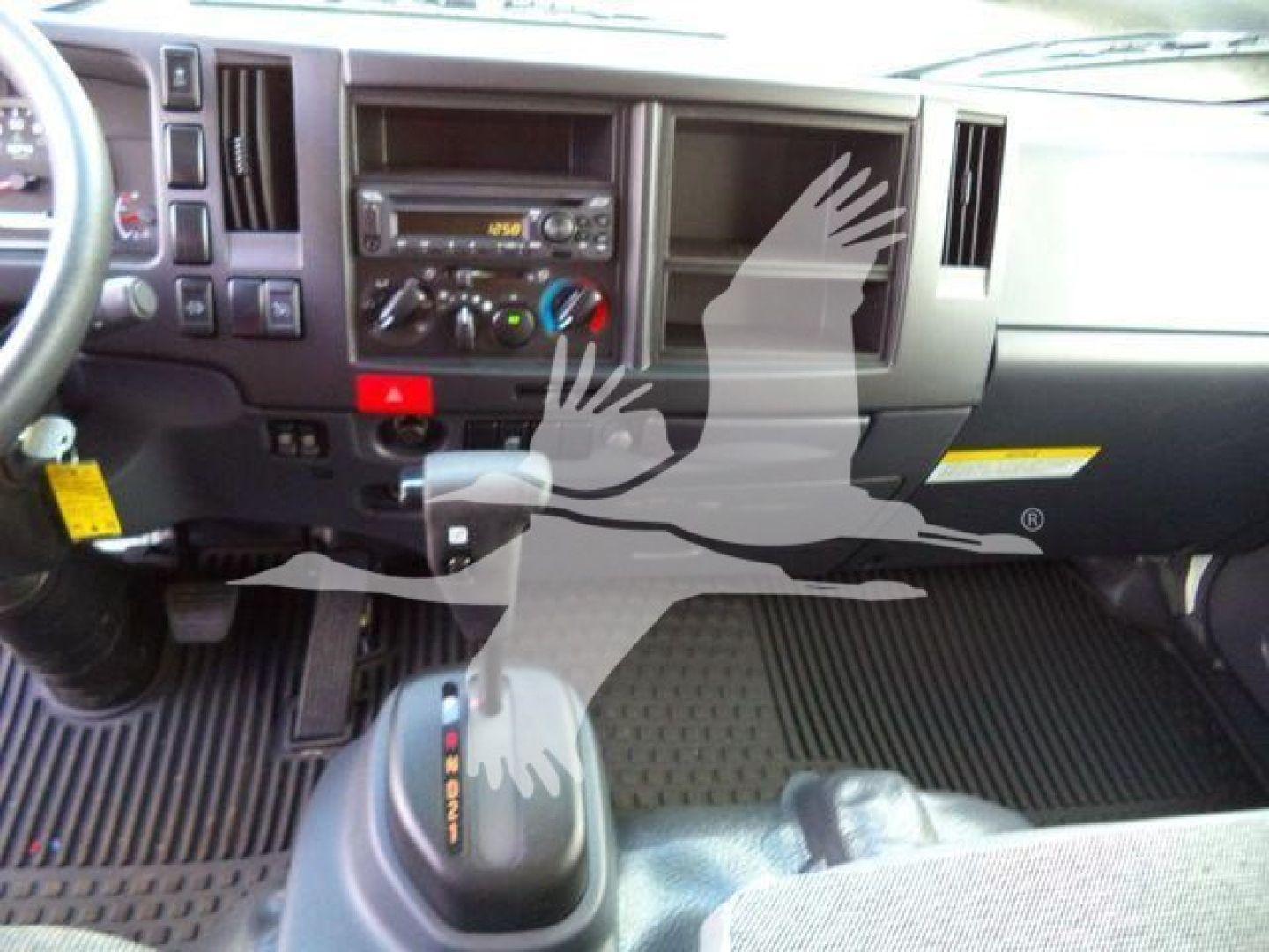 Isuzu NPR-HD truck dashboard and front interior showing steering wheel, center console with radio, climate controls, and gear shift; rubber floor mats visible.